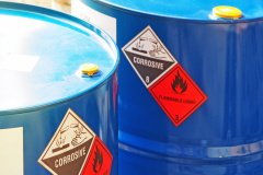 the close-up shot of blue color hazardous dangerous chemical barrels ,have warning labels of corrosive & flammable liquid in daylight on daytime.